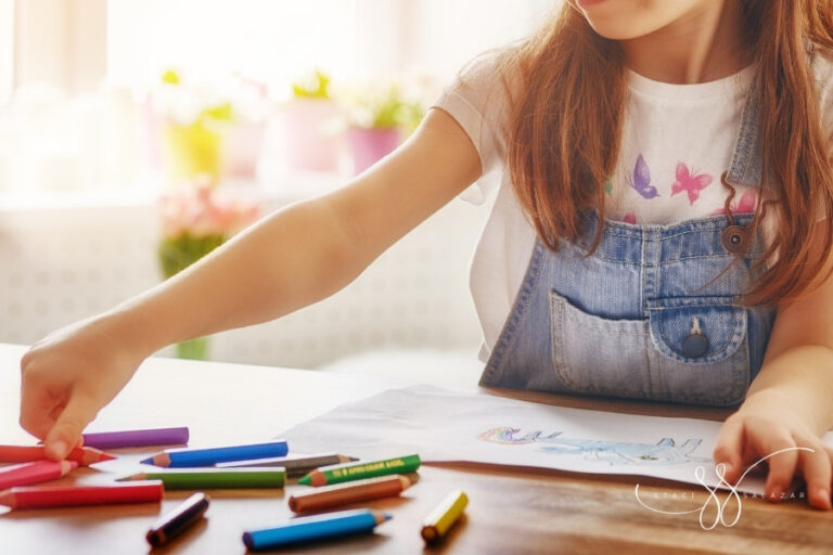 brunette child using colored pencils to draw a unicorn