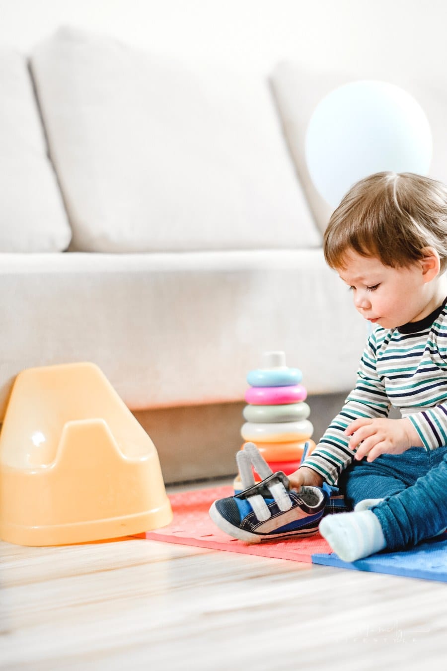 toddler putting shoe on near a plastic training potty