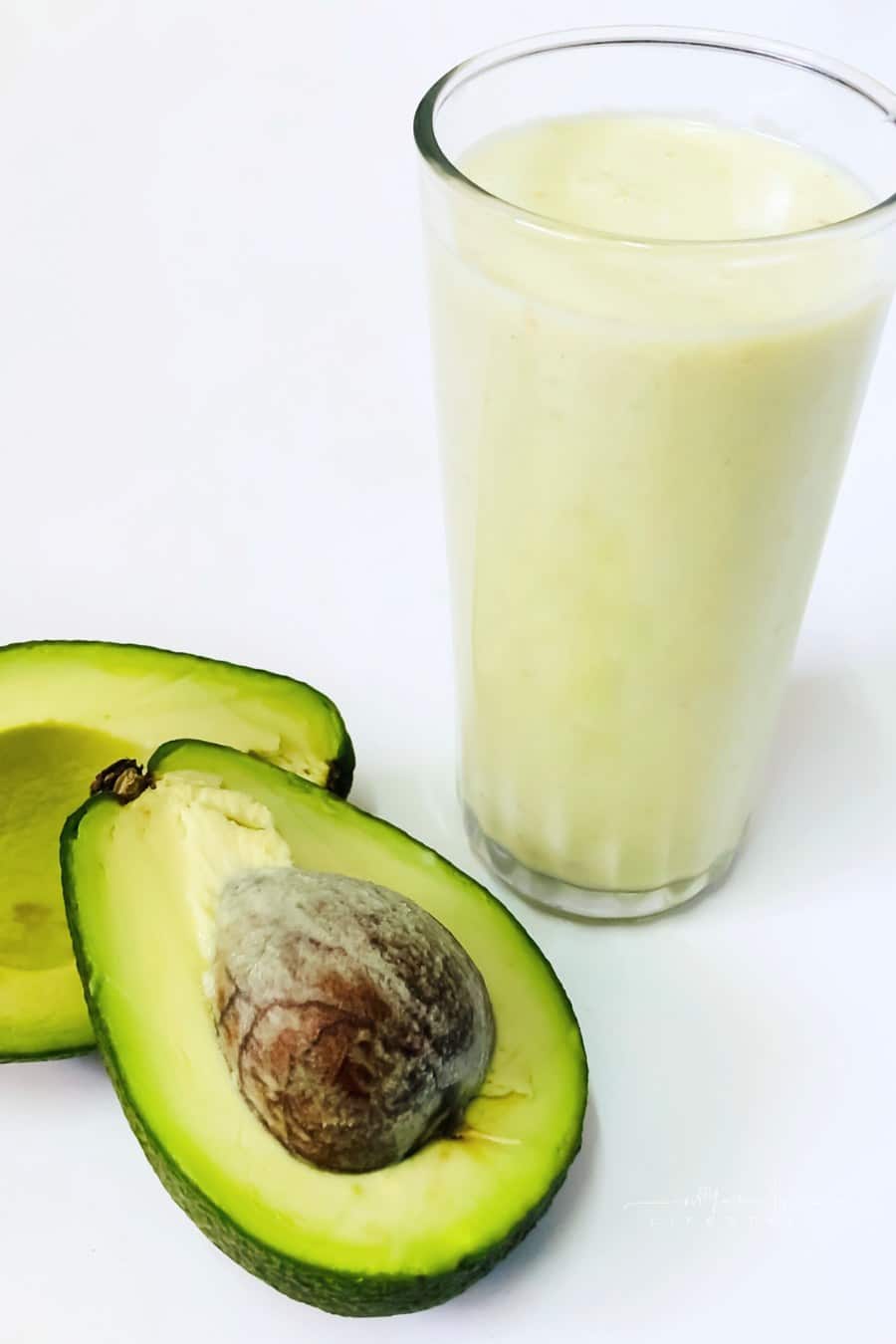 Glass of avocado coconut drink and sliced avocados