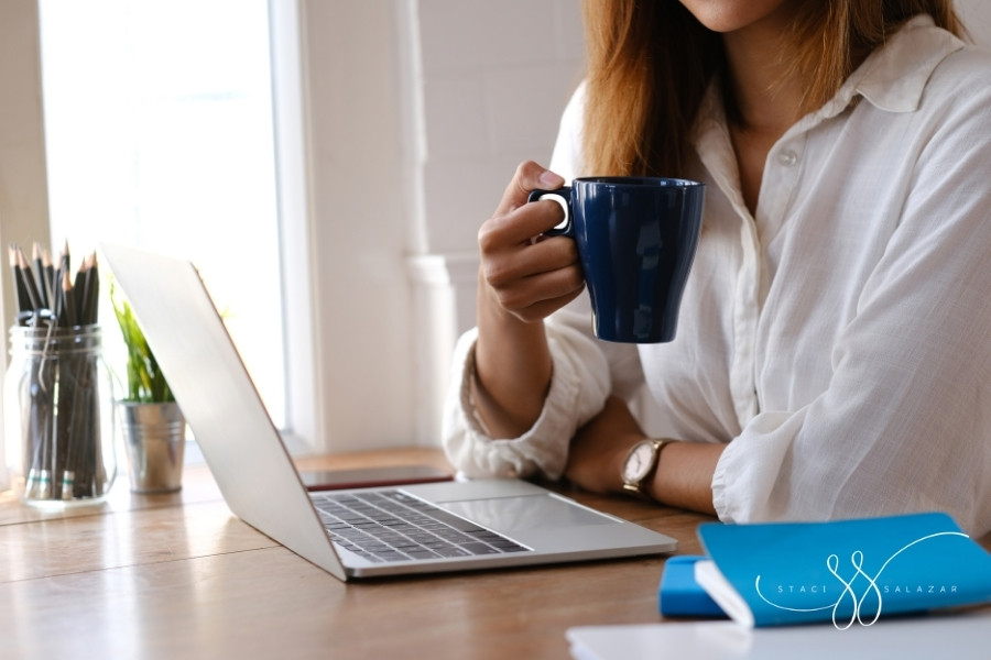 woman holding blue coffee mug over laptop with jar of pencils in background