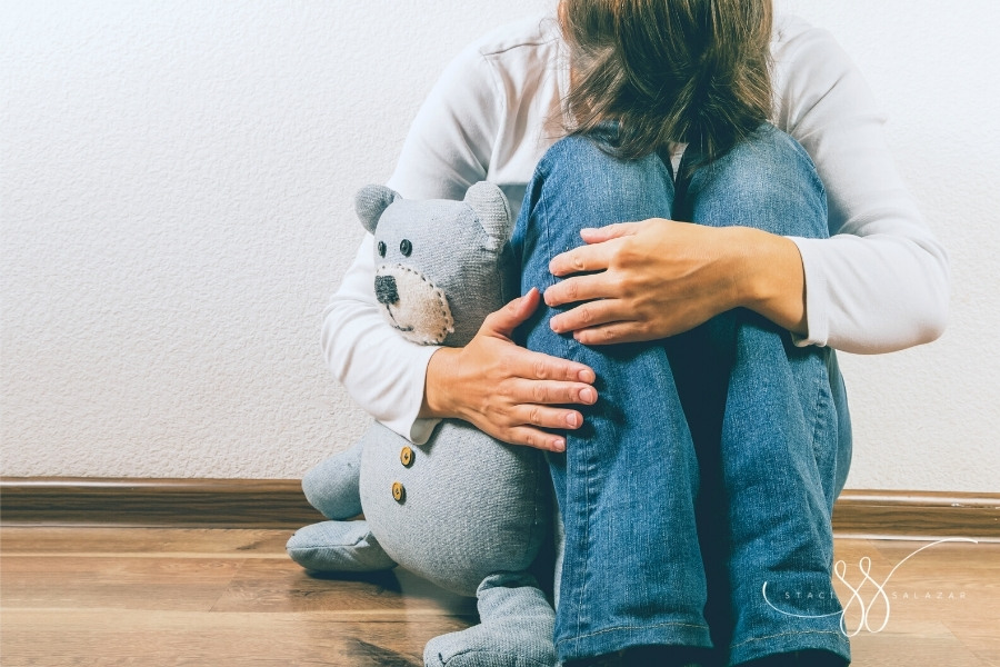 depressed woman with knees to her chest holding blue teddy bear miscarriage concept