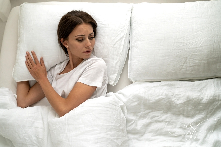 sad woman lying in bed alone looking at empty pillow beside her
