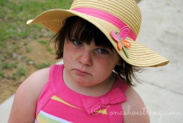 sad toddler frowning under a straw sun hat with a pink ribbon
