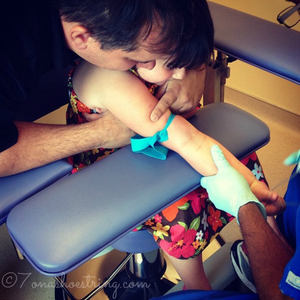 toddler getting blood drawn from her hand with dad holding her