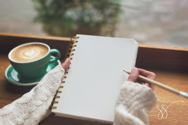 woman's hands holding pencil and blank journal in front of a cup of coffee