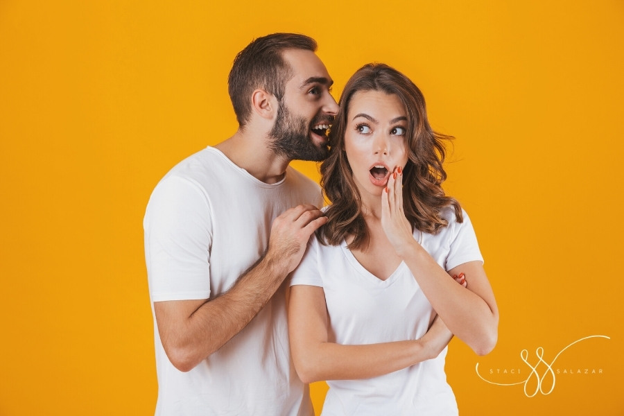 excited man whispering into woman's ear isolated over yellow background