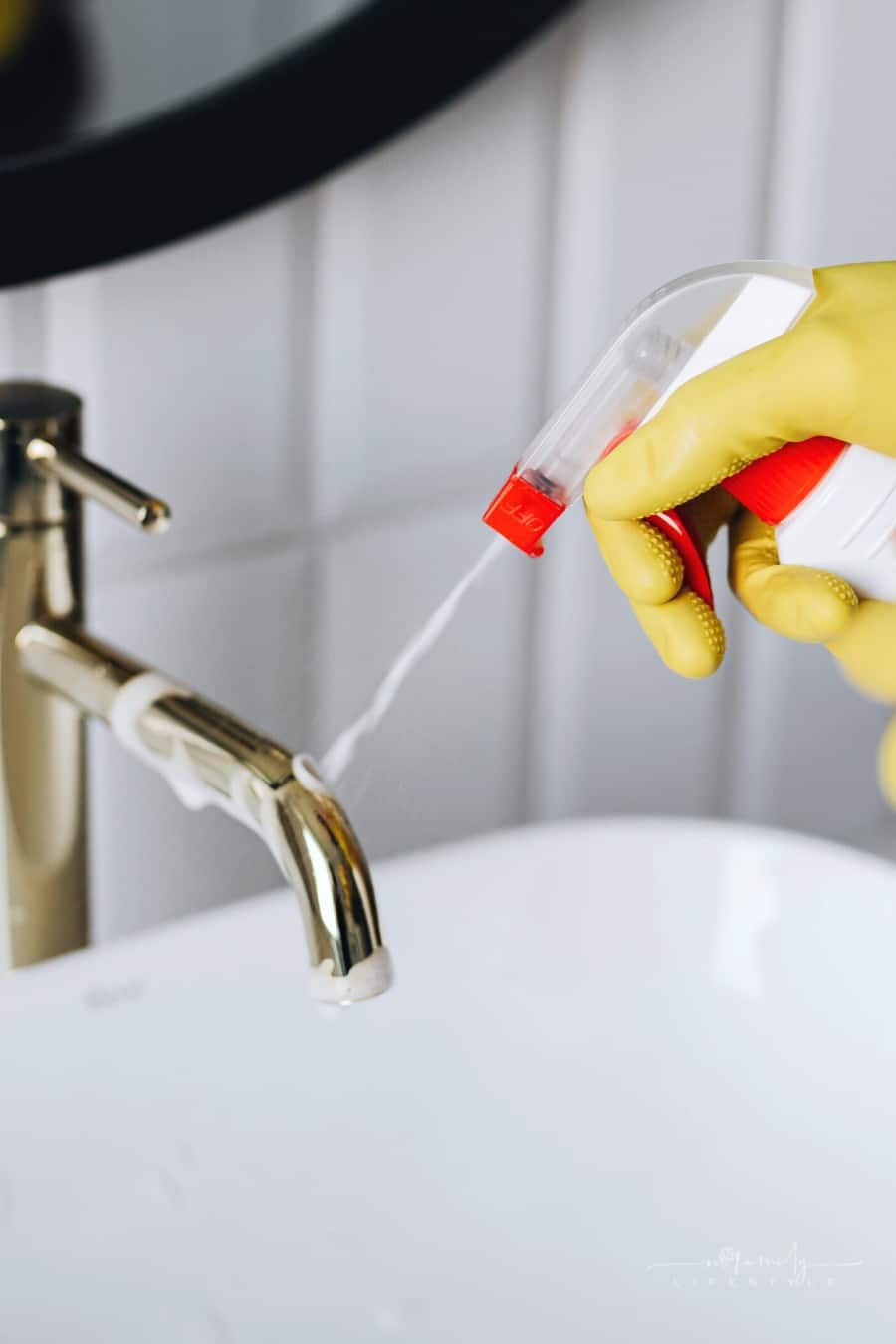 person spraying cleaner on bathroom faucet while wearing yellow gloves