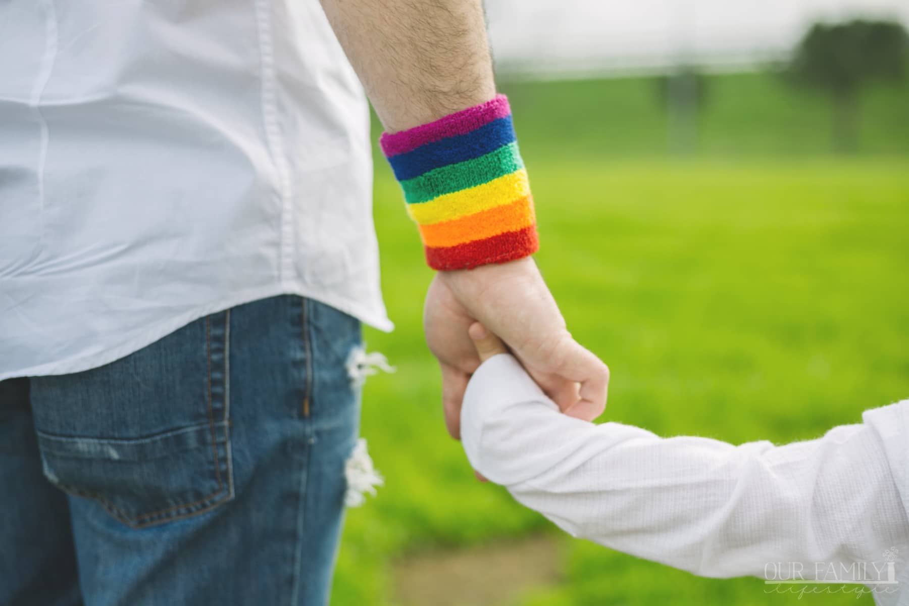 Father with rainbow wristband and his son walking in the park.