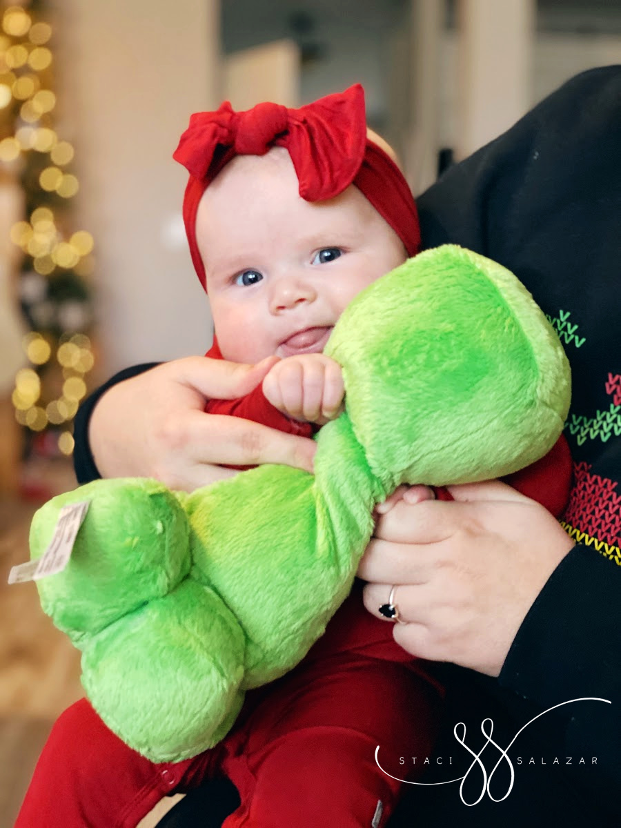 baby wearing red sleeper and bow holding a plush minecraft creeper