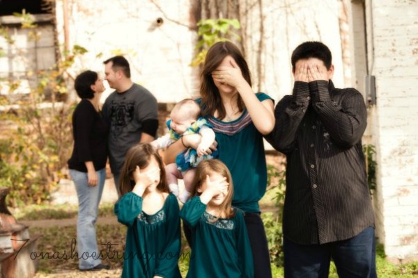 5 children holding hands over face in foreground with parents about to kiss in background