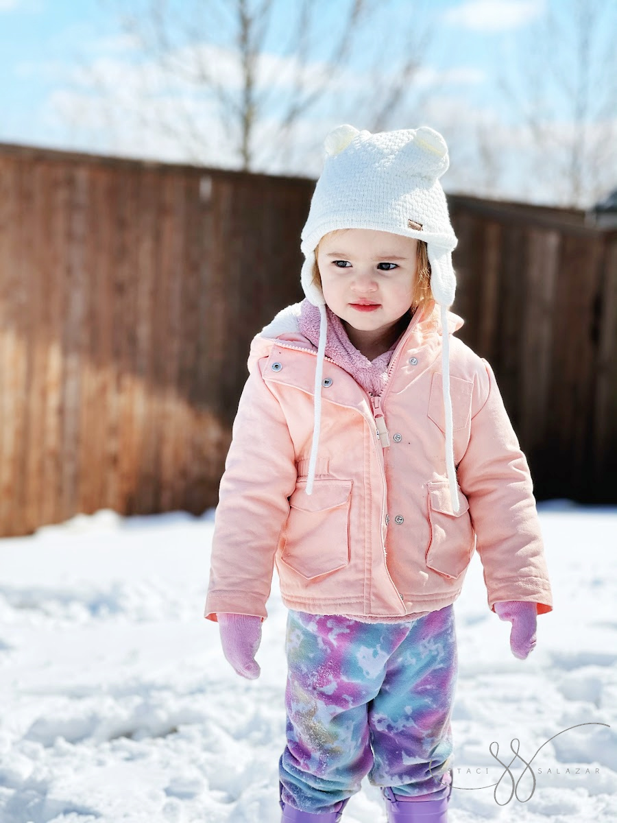 toddler standing in snow with pink socks on hands
