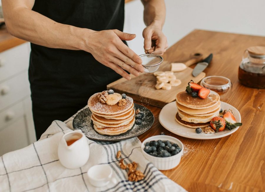 man dusting powdered sugar on pancakes with fresh berries and syrup.